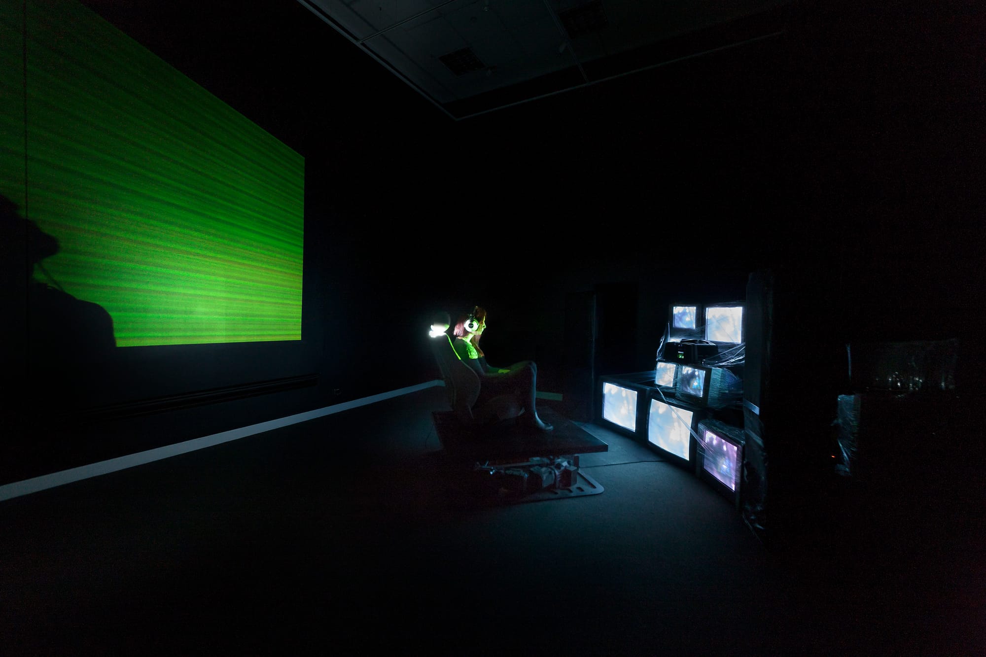 A person on a motion simulator chair in front of a wall of screens, wearing headphones